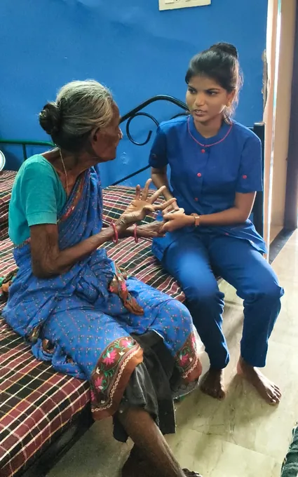 A nurse in blue speaking with an older woman and gently supporting her hands.