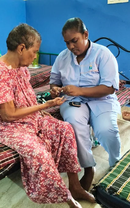 A nurse in light blue carefully supporting an older woman’s hand.