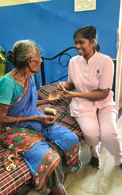 A smiling nurse in pink speaking with an older woman wearing a blue sari.