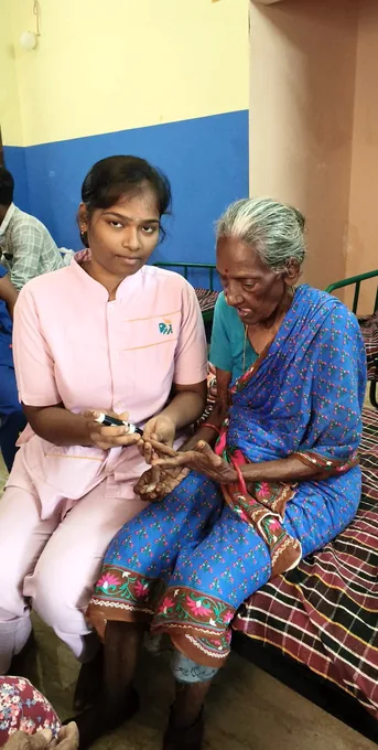 A nurse in pink holding the hand of an older woman wearing a blue sari.