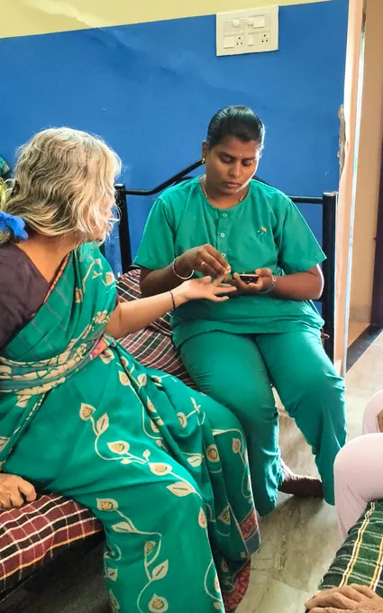 A nurse in green seated beside an older woman and attending to her hand.